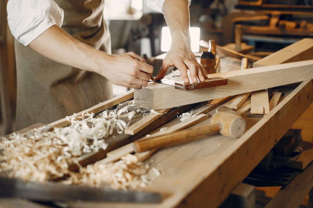 Apprenti en menuiserie travaillant sur une pièce de bois dans l’atelier partagé des Ateliers CRAAFT à Lille.